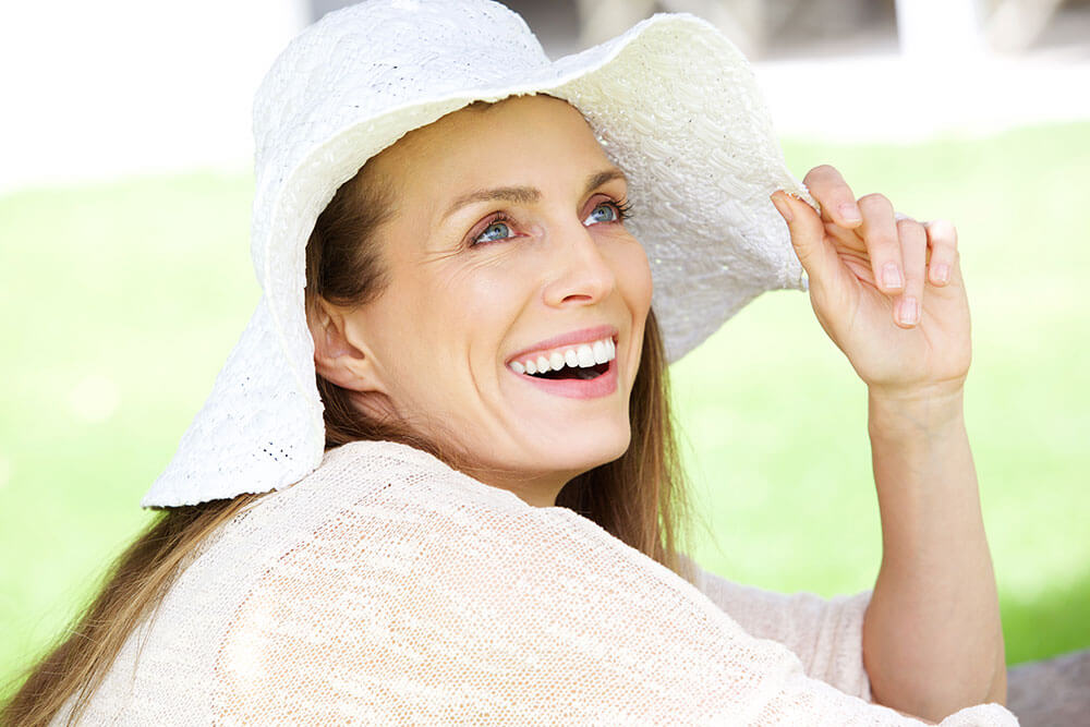 Smiling woman wearing a floppy white hat and white shirt